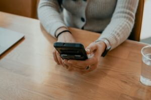 wiretap Massachusetts woman in grey long sleeve holding phone and looking at it wooden table