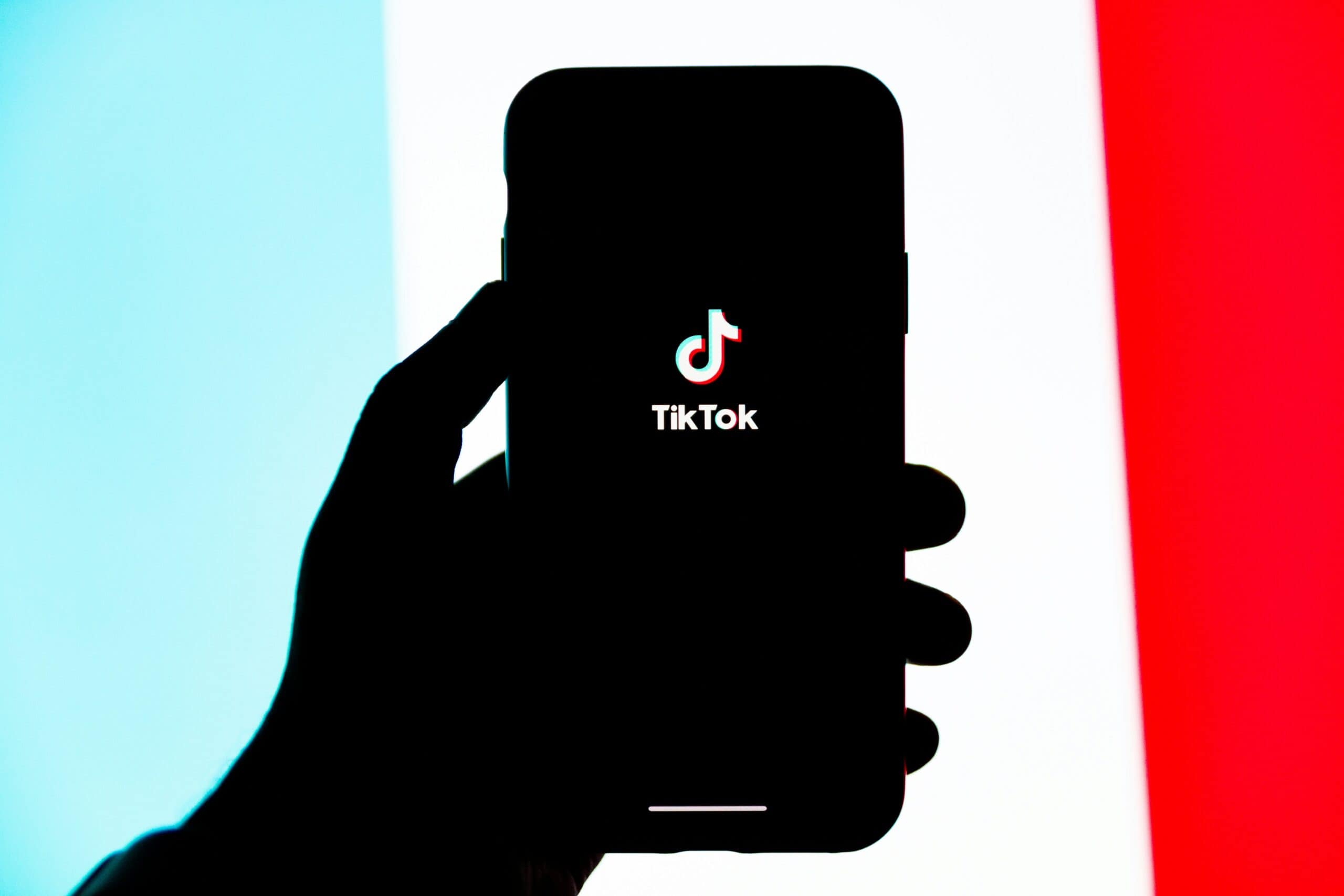 person holding phone with tiktok symbol in center of screen blue white and red background with black shadow outline of hand holding phone CIPA tikok claims