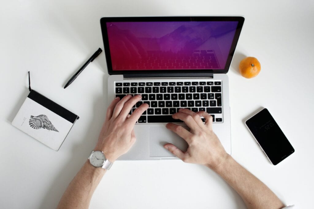 guy typing on macbook with an orange next to him email marketing