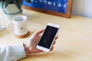 guy holding phone at a desk with a mug next to him TCPA telemarketing iphone