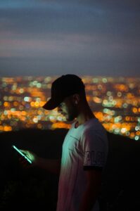 man with cap on looking at his phone at night with the city light up behind him possibly looks like california TCPA time telemarketing law telemarketers