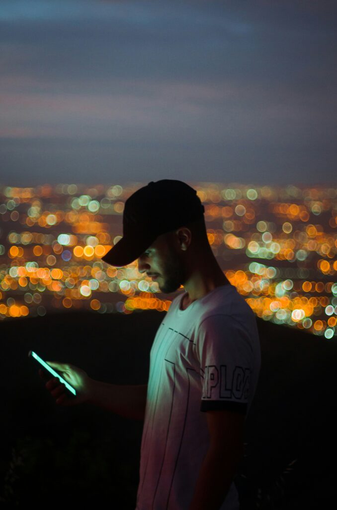 man with cap on looking at his phone at night with the city light up behind him possibly looks like california TCPA time telemarketing law telemarketers