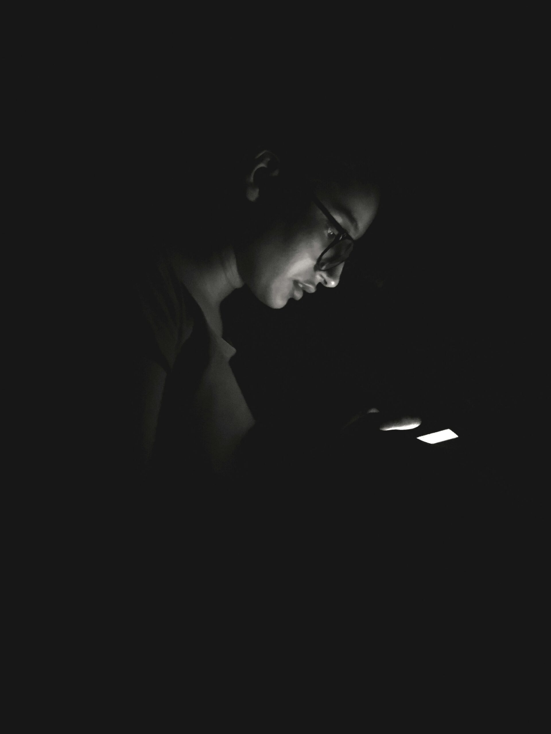 girl with glasses on looking at her phone at night